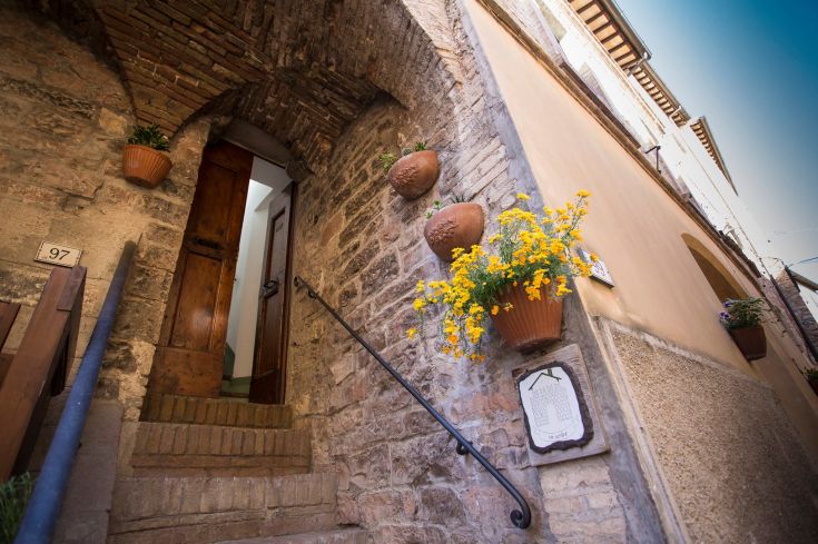 A stone entrance adorned with yellow flowers, typical of the historic center of an Umbrian village.