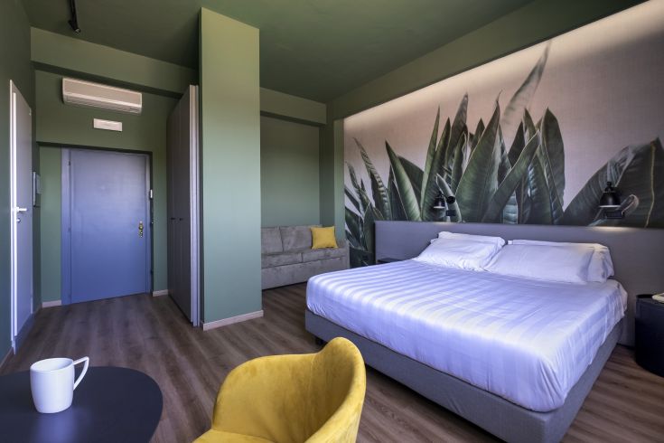 Modernes Zimmer in grünen Tönen mit einem Doppelbett und einem Sofa, ideal für einen ruhigen Aufenthalt.