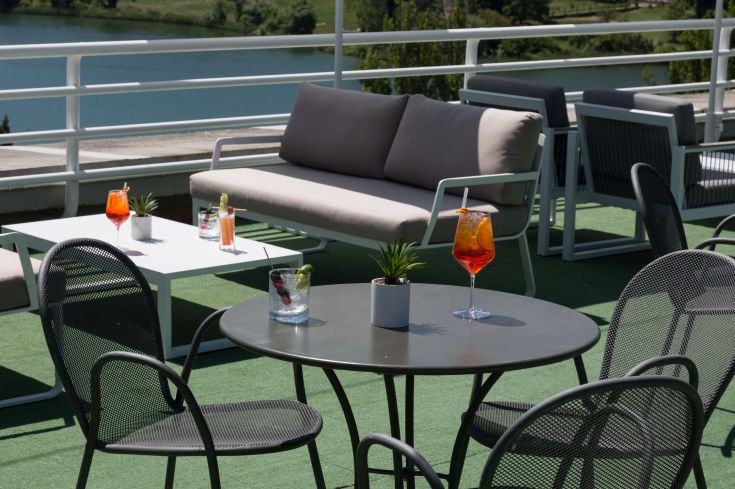 Eine Dachterrasse mit bunten Cocktails und modernem Dekor, mit Blick auf einen ruhigen See.