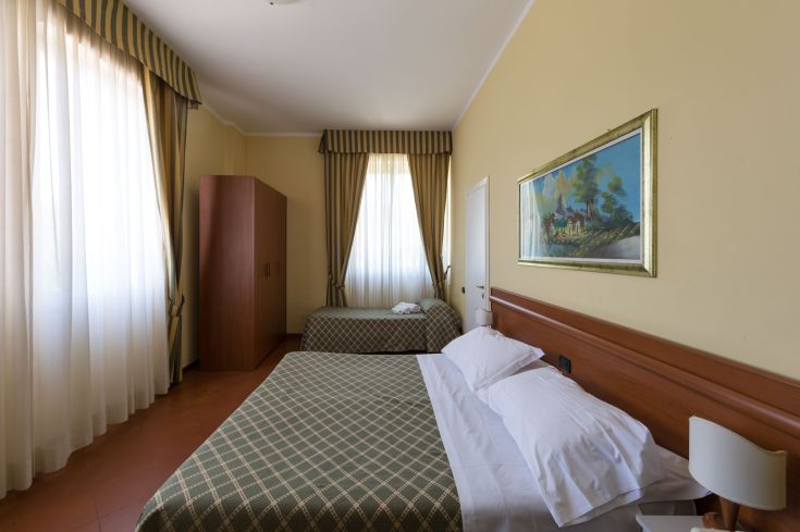 Einfaches Hotelzimmer mit zwei Betten, schlichter Einrichtung und Licht, das durch das Fenster strömt.