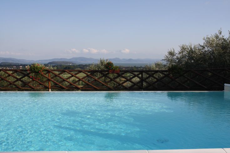 Una piscina ampia con vista su colline verdi, sotto un cielo sereno e circondata dalla vegetazione.