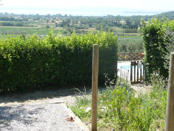 Panorama delle dolci colline che circondano il Lago Trasimeno, con vegetazione ben curata e piscine visibili.