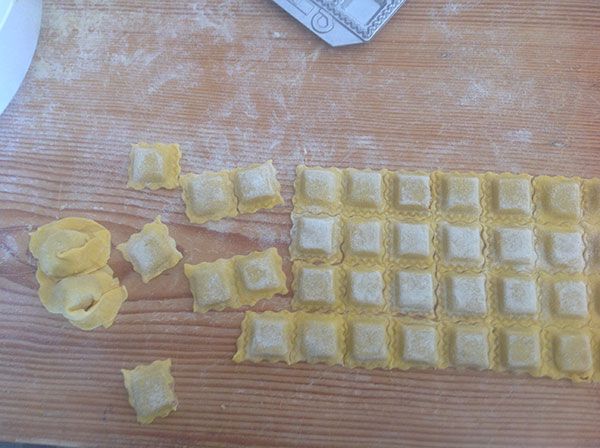 Ravioli freschi fatti a mano su un piano in legno infarinato, pronti per essere cotti.