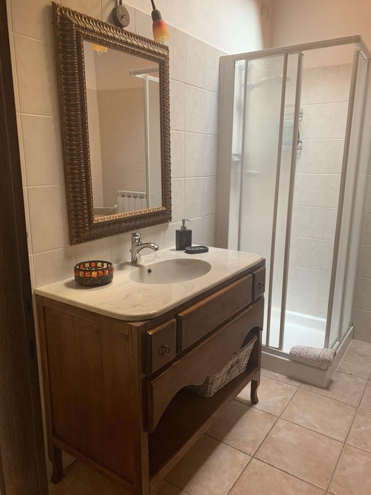 Bagno semplice con lavabo in legno, specchio e doccia in vetro trasparente.