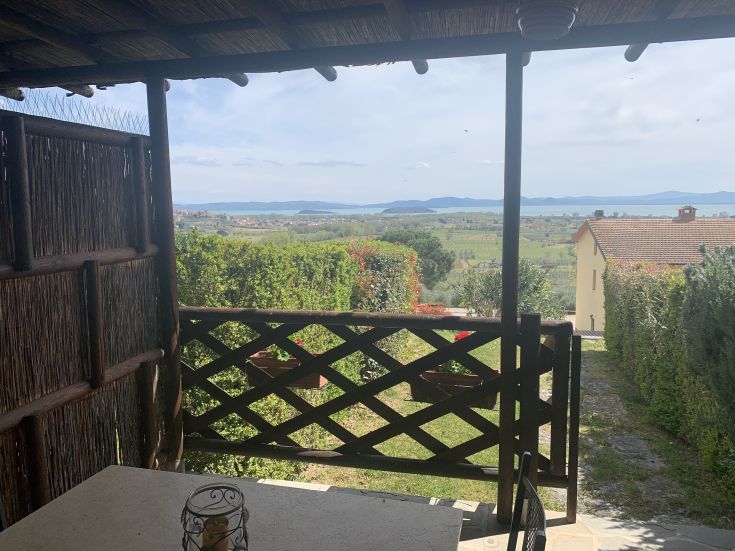 Panorama dal balcone di un agriturismo circondato da verde, con affaccio sul Lago Trasimeno.