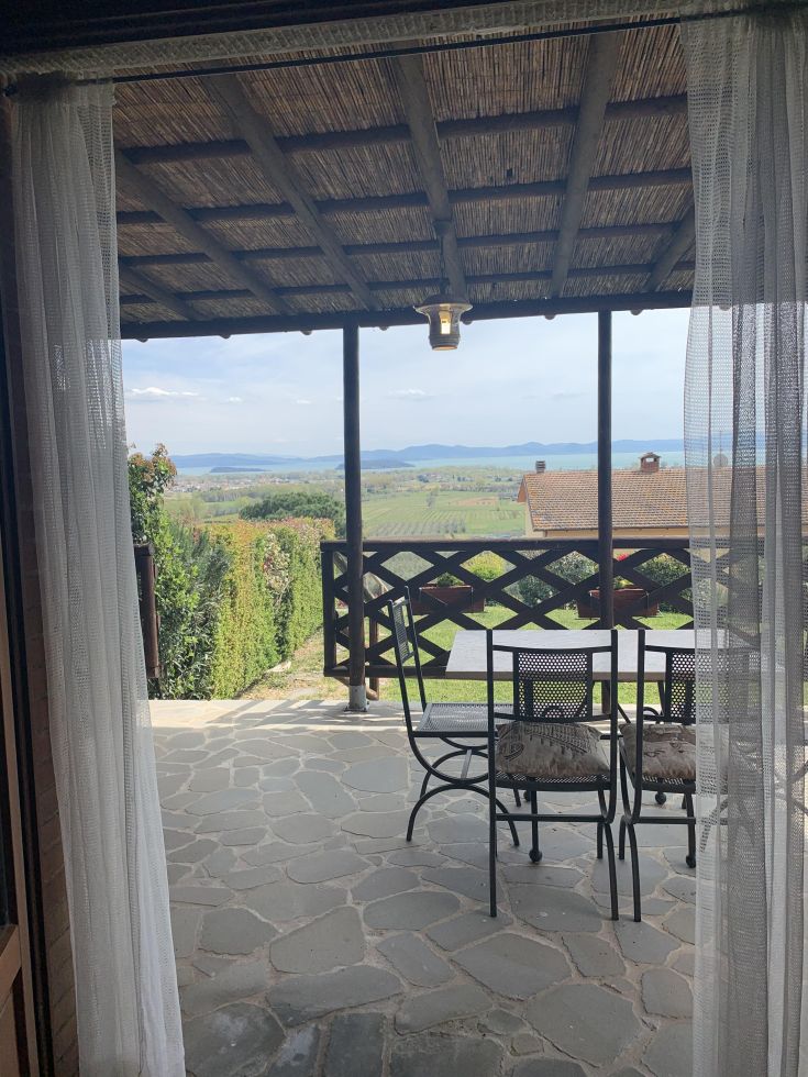 Panorama da un balcone attrezzato con tavolo e sedie, circondato dalla natura nei pressi del Lago Trasimeno.