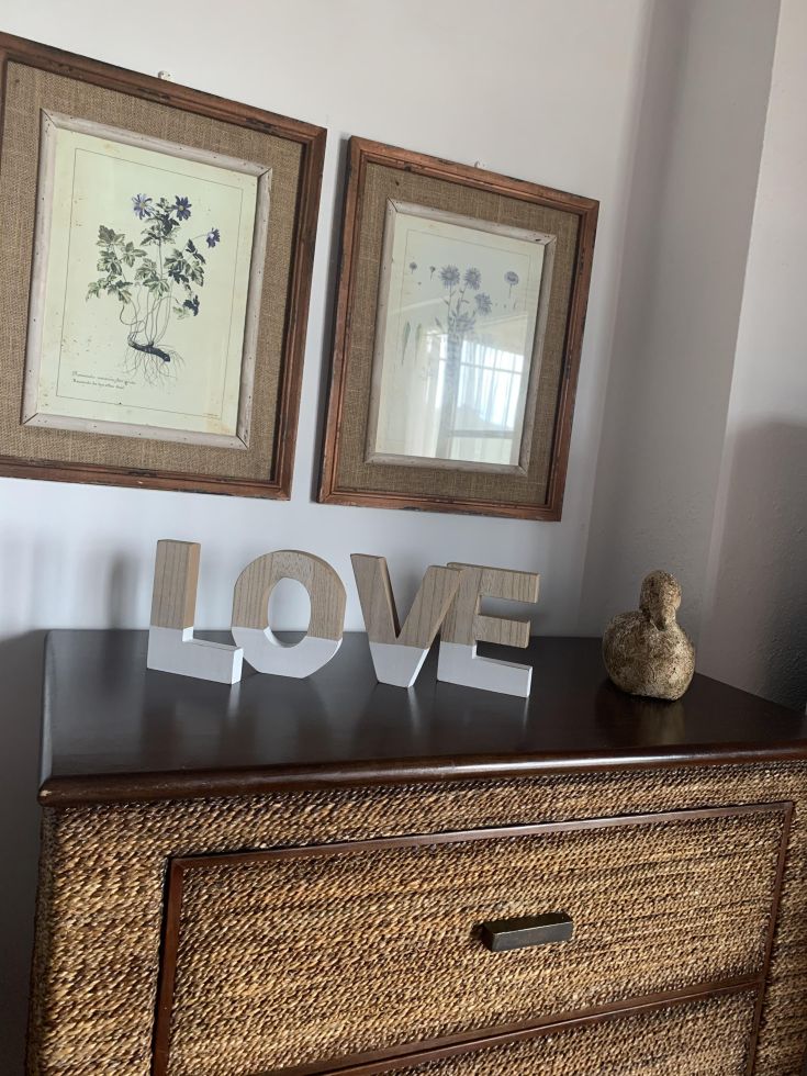 Decorazione con la scritta 'LOVE' su un mobile, accompagnata da quadri floreali sul muro.