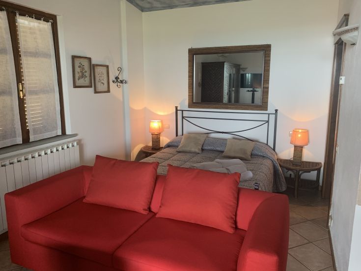 Una stanza ben arredata con un letto matrimoniale e un divano rosso, illuminata da lampade soffuse.