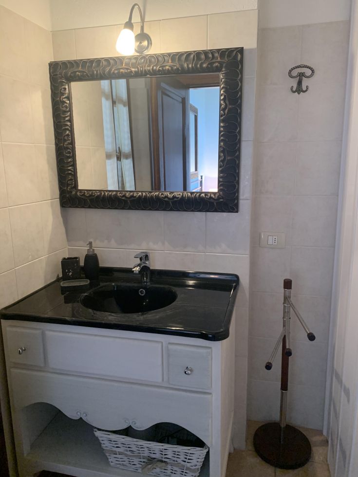 Bagno sobrio con specchio e lavabo in granito scuro, illuminato da una lampada a parete.