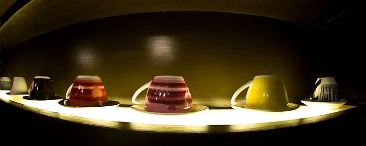 Tazze variopinte sistemate su un ripiano illuminato, donano un'atmosfera calda e accogliente all'ambiente.