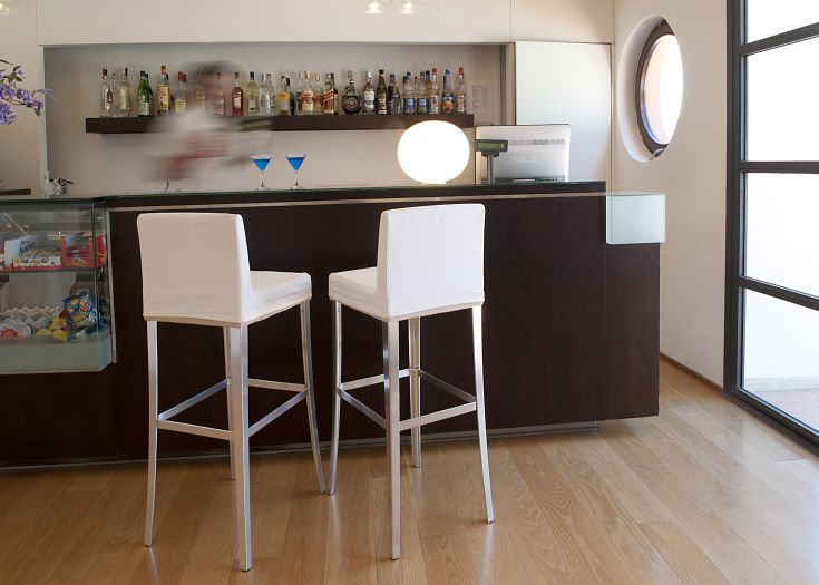Un ambiente curato con un bar moderno, sedie bianche e una selezione di bevande in mostra. Atmosfera tranquilla.