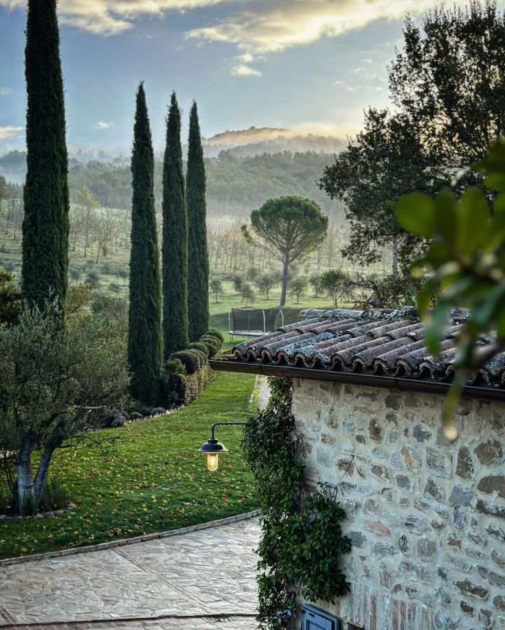 Une région rurale sereine avec des cyprès et une ferme en pierre.