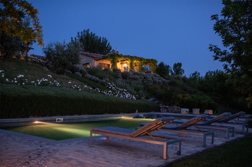 Evening scene of a villa with a swimming pool, surrounded by a garden filled with flowers and trees.