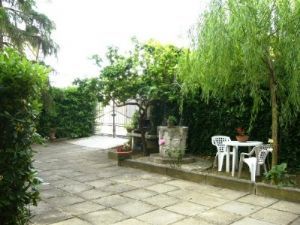 Kleiner Außenbereich mit einem hellen Tisch, umgeben von grünen Pflanzen und Rasen.