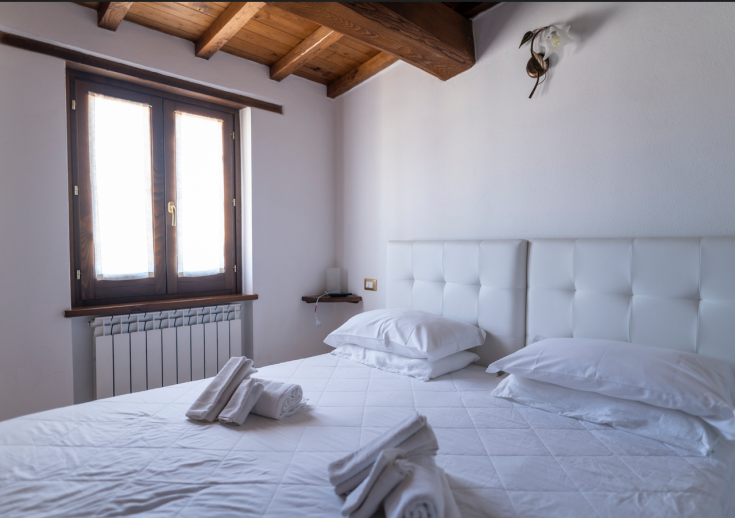 Camera semplice e accogliente in agriturismo, con letti bianchi e finestra che lascia filtrare la luce naturale.
