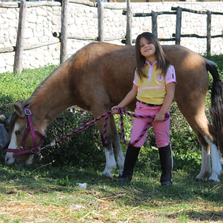 Una bambina gioca con il suo pony in un ambiente naturale sereno e tranquillo.