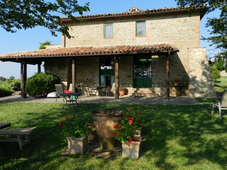 Un edificio in pietra con veranda e giardino, circondato da vegetazione.