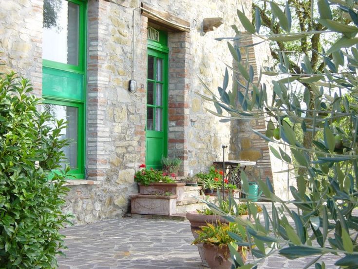 Un'entrata con porte verdi circondata da piante fiorite in uno spazio rustico.