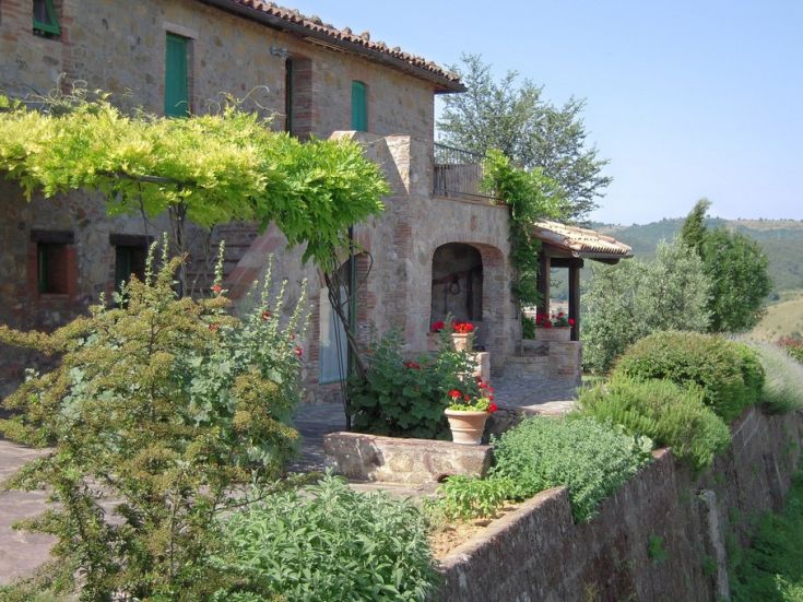 Una casa in pietra con piante e fiori che la circondano, situata in un ambiente verde e rilassante.