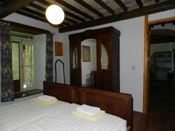 Camera semplice con letti matrimoniali e armadio in legno. Illuminata da una lampada a soffitto.