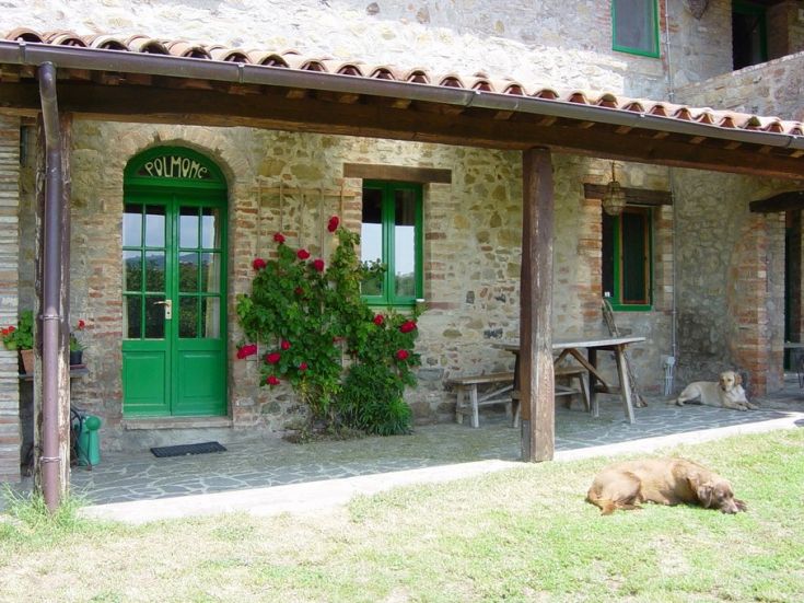 Una villa rustica con porte di colore verde e fiori, immersa nel verde della natura circostante.