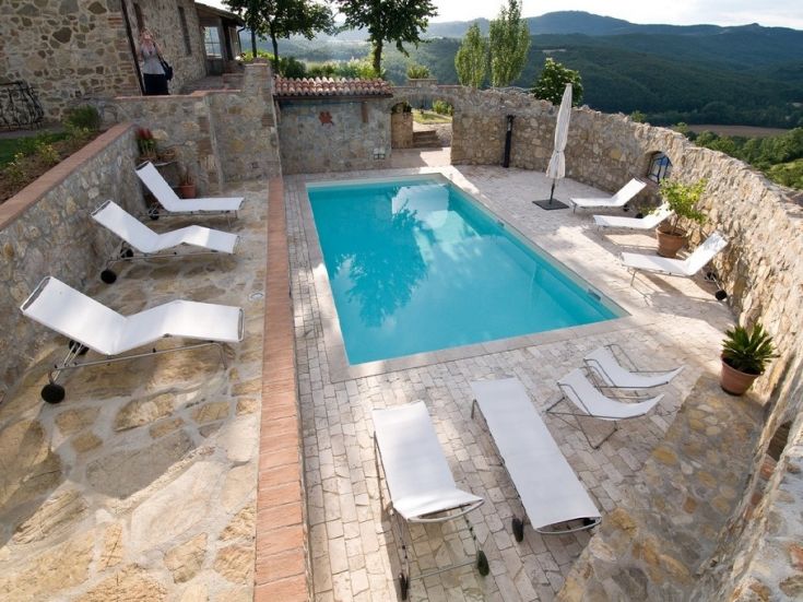 Una piscina situata in uno spazio esterno tranquillo, circondata da un ambiente naturale e arredamento semplice.