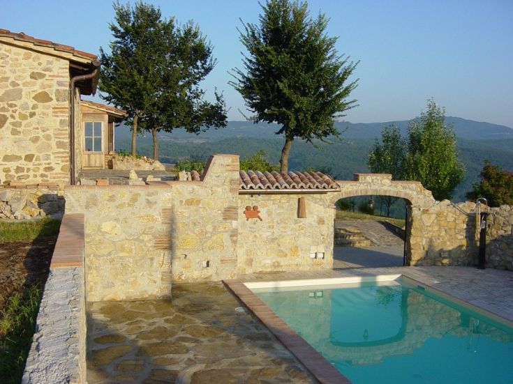 Edificio in pietra con piscina, circondato da colline verdi e un panorama tranquillo.