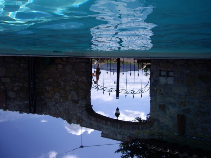 Un lago riflette un paesaggio tranquillo, con un cancello in ferro battuto e un cielo sereno.