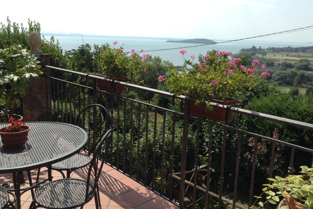 Scena sul Lago Trasimeno da una terrazza con fiori e un ambiente accogliente.