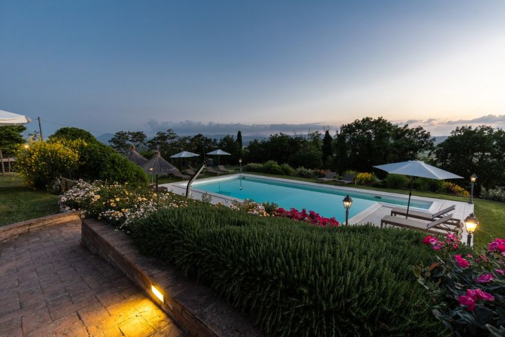 A sunset scene illuminating the agriturismo with a pool, surrounded by lush nature.