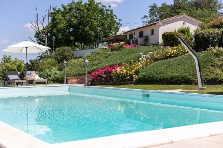 A peaceful pool area surrounded by greenery and colorful flowers at a farmhouse, perfect for relaxing in nature.