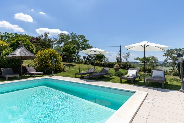 Relaxation area with a pool, loungers, and umbrellas, surrounded by nature in a peaceful setting.