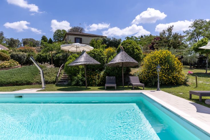 A pool surrounded by a lush garden, with a historic building in the background.