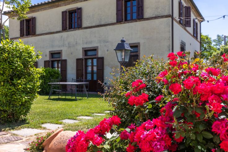 A rural building from the 1800s located in the lush Umbrian countryside, surrounded by plants and flowers.