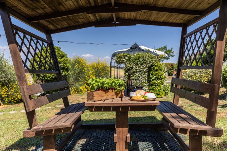 A cozy wooden gazebo with a picnic set up on a lush green lawn.