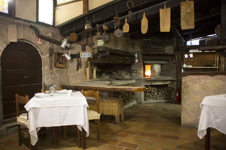 Intérieur d'un bâtiment rustique avec un mobilier simple et une cheminée allumée.