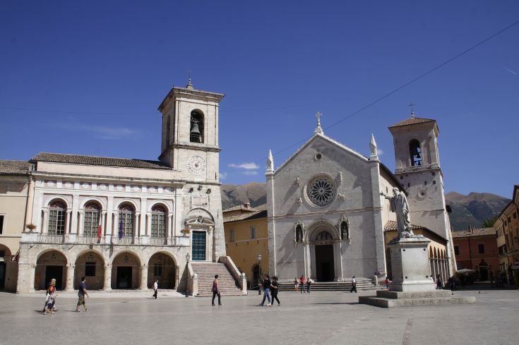 Ein zentraler Platz mit historischen Gebäuden und einer Statue, belebt von Menschen.