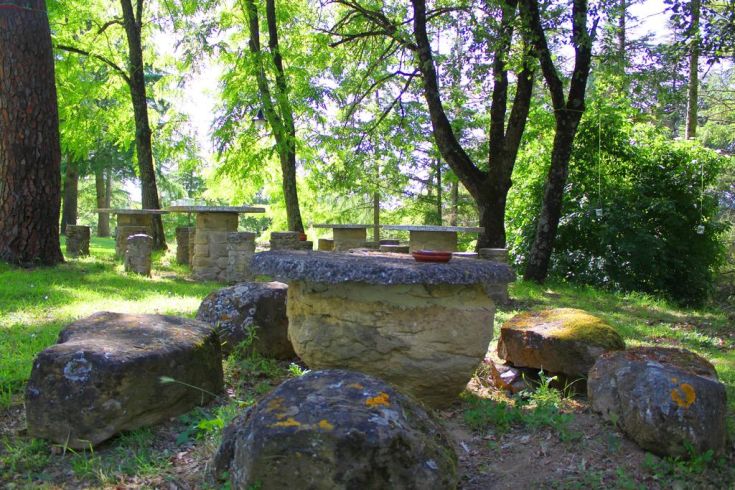 Outdoor area with stone tables and benches, surrounded by a peaceful natural environment.