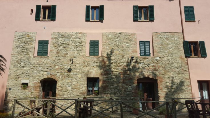 Edificio in pietra con finestre verdi scuro, immerso nel verde circostante.