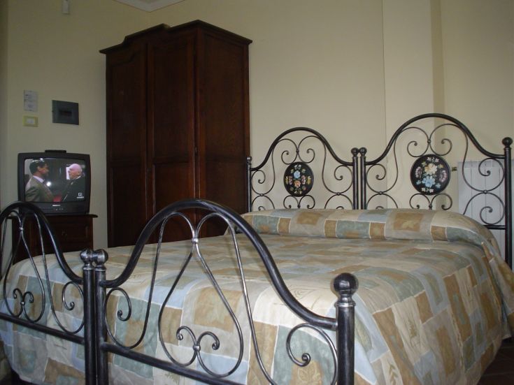 Chambre confortable de l'agriturismo avec un lit en fer et une télévision, dans un cadre simple et apaisant.
