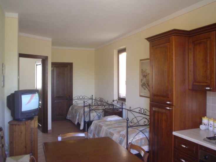 Un espace accueillant d'un agriturismo avec des lits en fer forgé, une table centrale et une cuisine fonctionnelle.