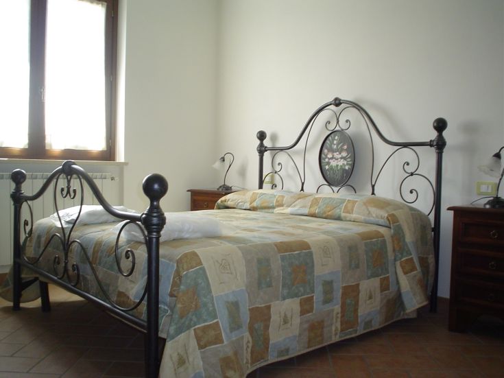 Chambre confortable dans un agriturismo, avec un lit en fer forgé et vue sur un paysage paisible.