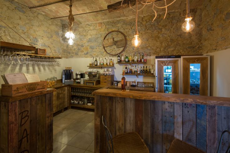 Interno di un bar semplice con arredamento in legno e dettagli in pietra, illuminato da luci soffuse.