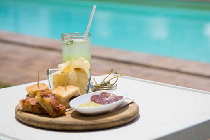 Un piatto assortito di antipasti accompagnato da una bevanda fresca di fronte a una piscina pulita.