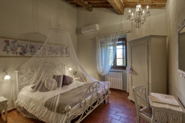 Stanza semplice con un letto a baldacchino, arredamento rustico e affacciata su un ambiente naturale.