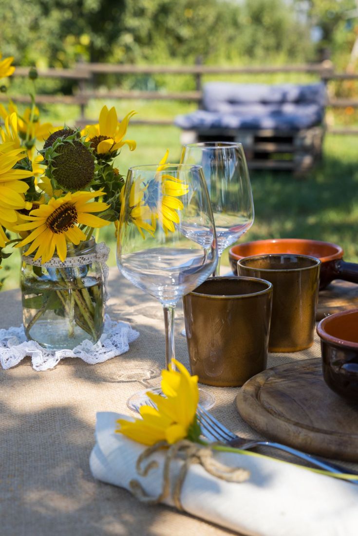 Un tavolo all'aperto allestito con girasoli freschi, bicchieri e posate, perfetto per un pranzo estivo informale.