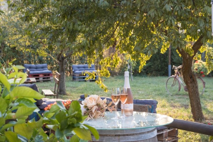 Un tavolo all'aperto con bottiglia di vino e fiori, circondato da un ambiente naturale di un agriturismo.