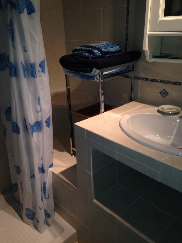 Ein einfaches Badezimmer mit blauen gestreiften Handtüchern, einer Dusche mit Vorhängen und hellen Details.