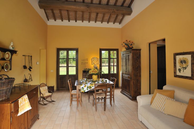 Simple agriturismo kitchen with yellow decorations and a window overlooking a green area.