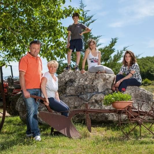 A group of people in a rural setting, surrounded by farming tools and green plants.